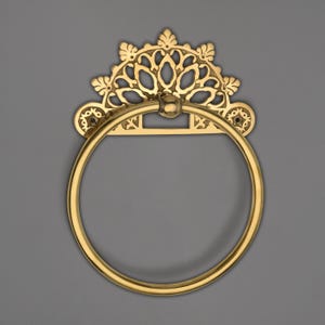 May include: A gold-colored towel ring with an ornate, decorative backplate. The backplate features a floral design with a semi-circular shape. The ring is circular and attached to the backplate with a small ball joint. The overall design is vintage.