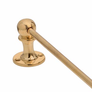 May include: A polished brass towel bar with a round base and a decorative ball finial. The bar extends horizontally from a central support, showcasing a classic design. The fixture is made of shiny, gold-toned metal.