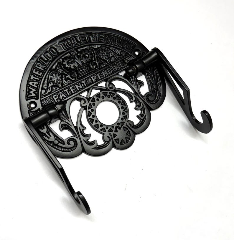 May include: Black cast iron toilet paper holder with ornate detailing and the text "Waterloo Toilet Fixture Patent Pending And".