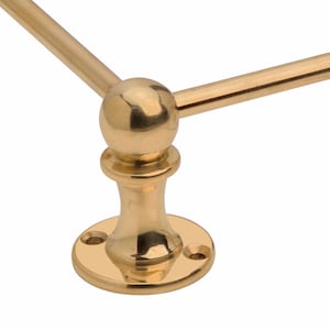 May include: A close-up of a gold-colored, decorative wall-mounted towel rack. The rack features a round base with three screw holes, a central support, and a spherical accent where the horizontal bars meet.