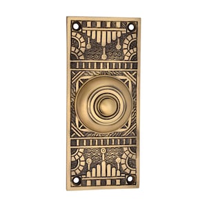 Op de afbeelding: Een rechthoekige messing deurbelknop met een Art Deco-ontwerp. De ronde knop is gecentreerd, omgeven door ingewikkelde geometrische patronen. Het messing heeft een warme, verouderde afwerking. Afmetingen: 15 cm x 7 cm.