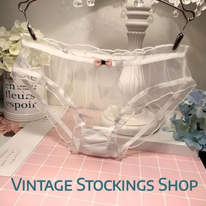 May include: White sheer underwear with a delicate design, featuring a small pink bow. The garment is displayed on a pink and white checkered surface. The text "VINTAGE STOCKINGS SHOP" is visible at the bottom.