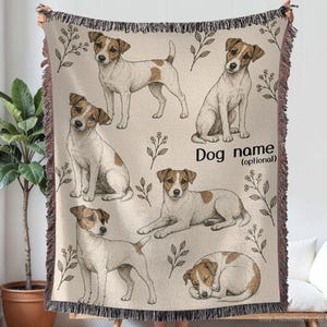 Może przedstawiać: Tkany koc z beżowym tłem, ozdobiony wieloma ilustracjami terierów Jack Russell w różnych pozach. Koc posiada motywy botaniczne, frędzle na krawędziach oraz nadrukowany tekst Dog name (optional) po prawej stronie.
