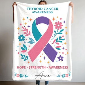 May include: White fleece blanket featuring a design for thyroid cancer awareness. The design includes a teal, pink, and purple ribbon, flowers, stars, and the words "Thyroid Cancer Awareness", "Hope Strength Awareness", and the name "Anne".