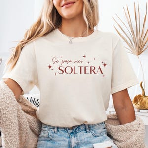 May include: A white t-shirt with the text "Se pasa rico SOLTERA" in brown lettering and small star accents.