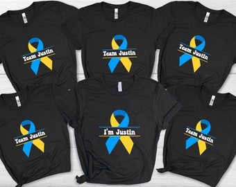 May include: Six black t-shirts featuring a blue and yellow ribbon design. The shirts display the text "Team Justin" or "I'm Justin".