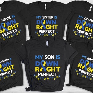Könnte beinhalten: Sechs schwarze T-Shirts mit einem blauen und gelben Band und dem Text "Mein [Familienmitglied] ist Down Right Perfect" auf jedem T-Shirt.