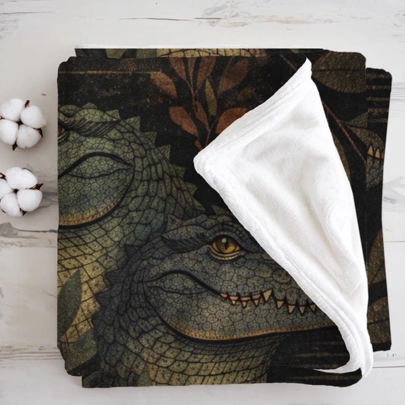 May include: A folded blanket featuring a detailed illustration of two alligators with yellow eyes and open mouths. The blanket has a dark background with green and brown foliage. The underside of the blanket is white.