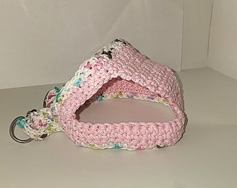 May include: A pink crocheted pet bed with a white and multi-coloured trim. The bed has a round opening and is made of soft yarn.