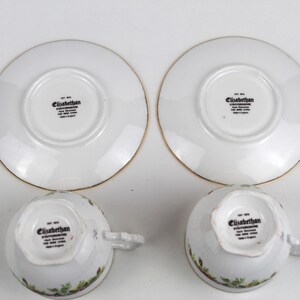 May include: Two white teacups and saucers with gold trim. The cups and saucers have a floral design around the edges. The text "Elizabethan" is printed on the bottom of the cups and saucers.