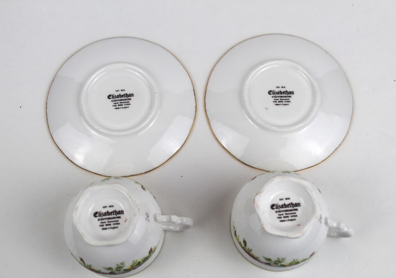 May include: Two white teacups and saucers with gold trim. The cups and saucers have a floral design around the edges. The text "Elizabethan" is printed on the bottom of the cups and saucers.