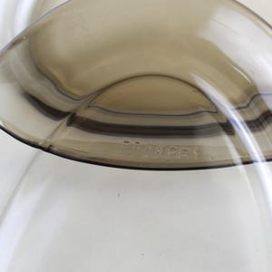 May include: Close-up of two overlapping, transparent, brown-tinted glass bowls. The bowls have a curved, organic shape. The text "FRANCE 1" is visible on the rim of one bowl. The bowls are set against a white background.