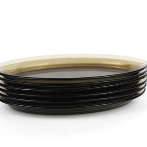 May include: A stack of six black glass plates with a light brown rim. The plates are round and have a simple, modern design. The plates are stacked on top of each other against a white background.