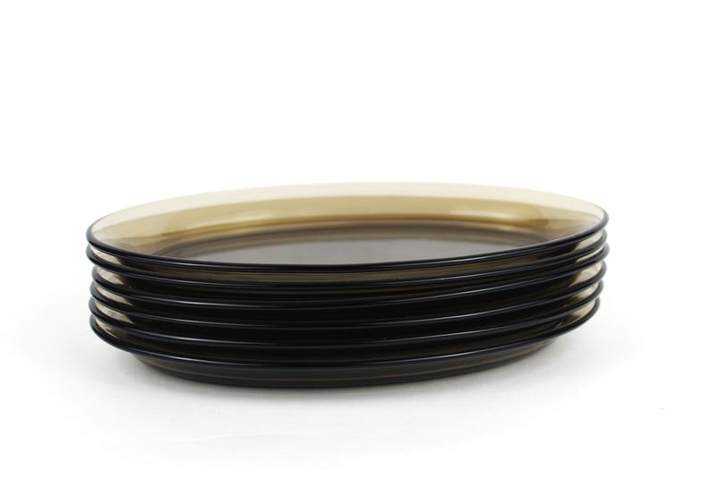 May include: A stack of six black glass plates with a light brown rim. The plates are round and have a simple, modern design. The plates are stacked on top of each other against a white background.