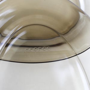 May include: Close-up of a transparent, curved glass object with a light brown tint. The word "-coroc" is subtly etched into the glass. The design features smooth, flowing lines and a minimalist aesthetic.