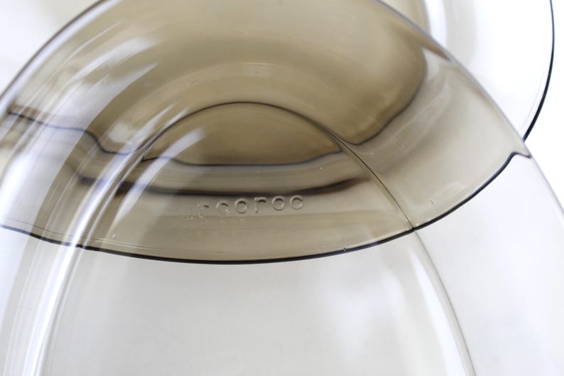 May include: Close-up of a transparent, curved glass object with a light brown tint. The word "-coroc" is subtly etched into the glass. The design features smooth, flowing lines and a minimalist aesthetic.