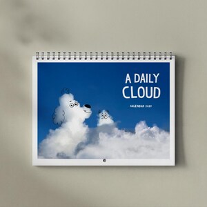 May include: A spiral-bound wall calendar titled A DAILY CLOUD CALENDAR 2027. The cover features a bright blue sky with white clouds shaped like a dog and a cat, with simple black line drawings added to define their faces and features.