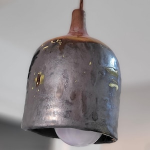 Könnte beinhalten: Eine glockenförmige Keramik-Hängeleuchte mit einer dunklen, gesprenkelten anthrazit- und braunfarbenen Glasur. Die Oberfläche weist unregelmäßige metallisch goldfarbene Akzente und ein glattes, glänzendes Finish auf. Eine weiße Glühbirne ist sichtbar.