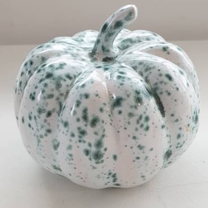 May include: A white ceramic pumpkin with green speckles. The pumpkin has a smooth, glossy finish.
