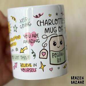 May include: White ceramic mug with a colorful design featuring the text "Charlotte's Mug of Positivi-Tea" and other motivational phrases like "You are amazing" and "Keep going".