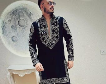 May include: A man wearing a black long-sleeved shirt with silver embroidery and black pants. He is wearing sunglasses and has a beard.