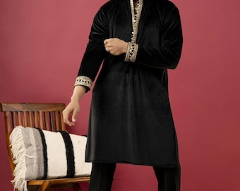 May include: Black velvet tunic with gold embroidery on the collar and cuffs. The tunic is paired with black pants. The image shows a man wearing sunglasses and the outfit is suitable for formal occasions.