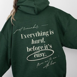 Puede incluir: Una sudadera con capucha verde oscuro con el texto "just remember - Everything is hard, before it's easy. from me to me - with love" impreso en la parte posterior.