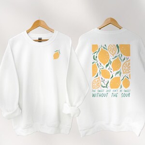 Könnte beinhalten: Weißer Pullover mit einem Zitronenmotiv auf der Vorderseite und einem Zitronenmuster mit dem Text "The sweet just isn't as sweet without the sour" auf der Rückseite.