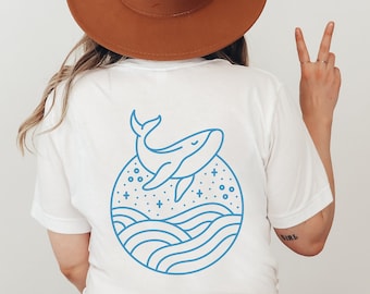 May include: White t-shirt with a blue line drawing of a whale jumping out of the water with stars and waves in a circle around it.