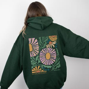 May include: Dark green hoodie with a floral design on the back. The design features large flowers in shades of pink, yellow, and orange, with green leaves and the text "NO RAIN, NO FLOWERS."