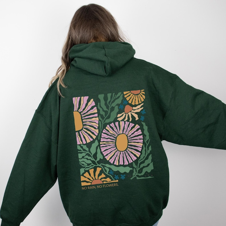 May include: Dark green hoodie with a floral design on the back. The design features large flowers in shades of pink, yellow, and orange, with green leaves and the text "NO RAIN, NO FLOWERS."