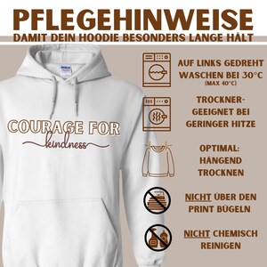 Może przedstawiać: Biała bluza z kapturem z napisem "COURAGE FOR kindness" w brązowych i bordowych literach. Po prawej stronie obrazu znajdują się instrukcje dotyczące pielęgnacji, w tym instrukcje prania, suszenia i prasowania.
