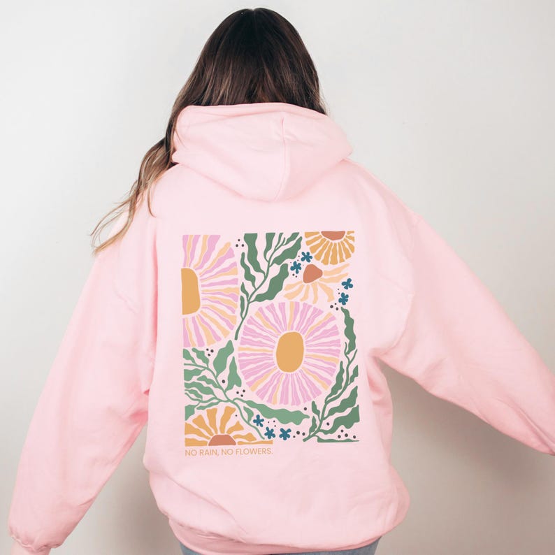 May include: A pale pink hoodie with a floral design on the back. The design includes large pink and yellow flowers, green leaves, and small blue flowers. The text "NO RAIN, NO FLOWERS" is printed at the bottom of the design.