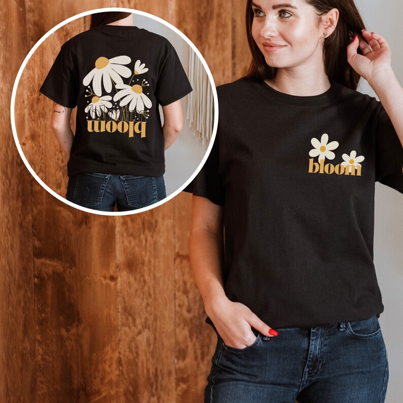 May include: Black t-shirt with a floral design and the word "bloom" in yellow. The front of the shirt features two white daisies with yellow centers and the word "bloom". The back of the shirt has a larger floral design with the same text.