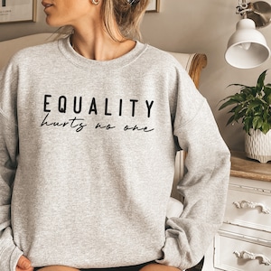 Könnte beinhalten: Ein grauer Pullover mit dem Aufdruck "EQUALITY hurts no one" in Schwarz.