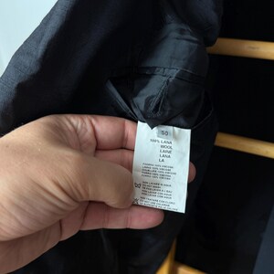 May include: Black jacket interior with a tag showing fabric composition: 100% wool. The tag also includes washing instructions and the size 50.