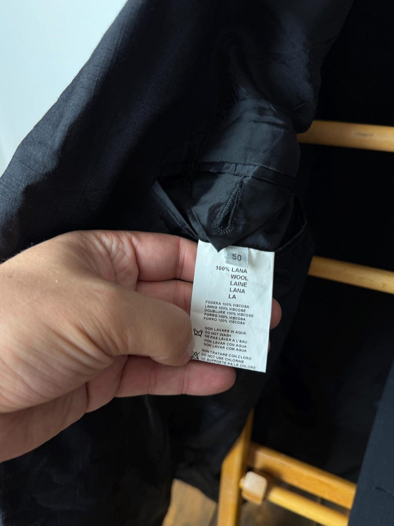 May include: Black jacket interior with a tag showing fabric composition: 100% wool. The tag also includes washing instructions and the size 50.