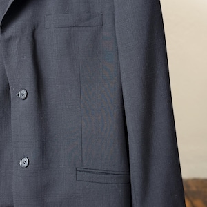 May include: A dark navy blue blazer with a subtle plaid pattern. The blazer features two buttons and a chest pocket. The fabric has a textured appearance. The blazer is a classic style.