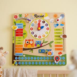 May include: A wooden educational wall calendar featuring the name Rosie, a central clock with colourful numbers, sliding markers for months, days of the week, and dates from 1 to 31. It includes illustrations of owls, a snail, a ladybug, and weather icons.