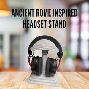 Pode incluir: Um suporte para fones de ouvido impresso em 3D de cor branca, inspirado na arquitetura romana antiga. O suporte possui uma coluna e um arco, e é projetado para segurar um par de fones de ouvido.