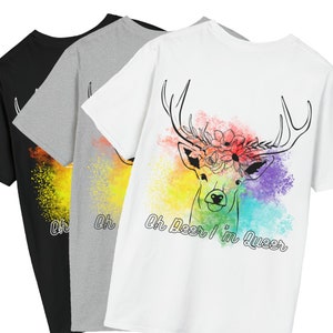 Puede incluir: Tres camisetas con un fondo de acuarela arcoíris y un dibujo en línea negra de un ciervo con una corona de flores. El texto "Oh Deer I'm Queer" está impreso en la camiseta blanca.