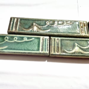 Peut inclure: Gros plan sur trois carreaux de céramique verts avec un motif ondulé décoratif et des accents dorés.