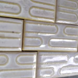 Puede incluir: Primer plano de baldosas de cerámica blanquecinas con acabado brillante. Cada baldosa presenta un diseño curvo empotrado en un color amarillo claro contrastante. Las baldosas están dispuestas en un patrón de cuadrícula, lo que sugiere una aplicación decorativa o funcional.
