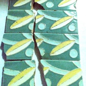 May include: A set of six teal green ceramic tiles with a repeating pattern of white and yellow stylized leaves and white circles. The tiles are broken into two pieces.