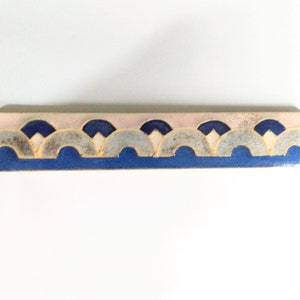 May include: A ceramic tile border with a repeating pattern of blue, white and grey arches. The tile has a pink background.