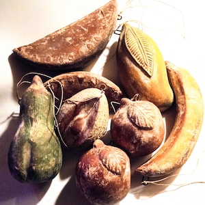 May include: A selection of vintage fruit decorations, including a banana, mango, apple, and pear. The ornaments are painted in earthy tones of brown, green, and yellow, with a distressed finish. Each decoration has a loop for hanging.
