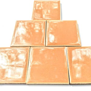 Könnte beinhalten: Sechs Terrakotta-farbene Keramikfliesen, die in Pyramidenform angeordnet sind. Die Fliesen sind glänzend und haben eine leicht unebene Oberfläche.