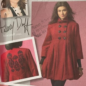 May include: McCall's sewing pattern M5513 for a red double-breasted coat with a pleated skirt and high collar. The envelope features photos of the coat, including a back view with dark floral embroidery and a plaid-lined interior detail.