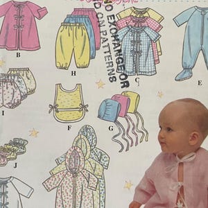 Puede incluir: Patrón de costura Simplicity 9380 para canastilla de bebé en tallas NB, S, M y L. El sobre muestra ilustraciones de varias prendas infantiles incluyendo bata, pantalones, babero, gorrito y pijama con pies, junto a la foto de un bebé en rosa.