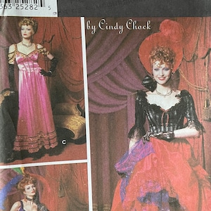 May include: Simplicity Costumes sewing pattern for a saloon girl costume. The pattern includes three different looks: a pink dress with a lace trim, a black and purple dress with a lace trim, and a red skirt with a lace trim and a black top. The pattern is for sizes 14, 16, 18, and 20.